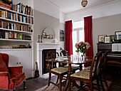 Polished dining table and bookshelves with red velvet curtains and armchair in contemporary London home   England   UK