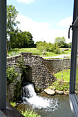Blick auf Steinbrücke und Wehr aus dem Fenster eines ländlichen Bauernhauses in Großbritannien