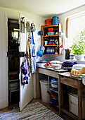 Homeware at sunlit window with aprons on back of door in Brabourne farmhouse kitchen,  Kent,  UK