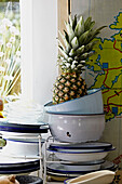 Pineapple on stacked metal bowls at sunlit kitchen window of Brabourne farmhouse,  Kent,  UK
