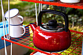 Bright red kettle on folding shelf in Brabourne farmhouse garden,  Kent,  UK