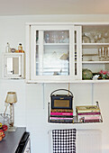 Radio and books below glass fronted wall cabinet in Faversham kitchen,  Kent,  UK