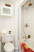 Dusche mit Messingarmatur und Toilette im weiß gefliesten Badezimmer eines Hauses in Faversham, Kent, Großbritannien