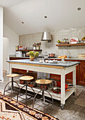 Three barstools at salvaged island unit in farmhouse kitchen of London home  UK