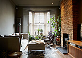 Sofa and ottoman with buttoned brown leather rocking chair in bay window of East London townhouse  England  UK