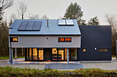 Beleuchteter Neubau mit Sonnenkollektoren in einem Waldgebiet in Devon (UK)