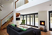 Black sofa with bright green cushions at lit fire in open plan  double height Devon new build  UK