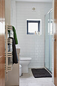Handtücher auf dem Heizkörper mit Badematte in der Duschkabine und quadratischem Fenster in einem Neubau in Devon, Großbritannien