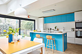 Vases of flowers on yellow table in  modernised fitted turquoise  kitchen extension  London  UK
