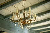 Gilt and glass chandelier against traditional French pastel blue ceiling beams and limed floorboards