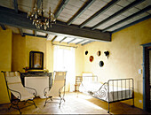 Traditionelles französisches Schlafzimmer in sonnigem Gelb und Pastellblau mit modernen dekorativen Eisenstühlen und Einzelbett