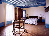 Master bedroom in French style with terracotta floor tiles and pastel blue beams