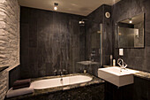Dark slate tiled bathroom with marble bath surround and white bath and basin