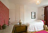 Einzelbett in einem Zimmer mit eingebautem Stauschrank und floral gemusterter Wand in einem Haus in New Malden, Surrey, England, UK