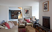 Sesselpaar und Sofa mit Korbhockern am Kamin in einem Haus in Essex UK