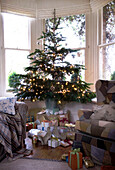 Christmas tree with presents underneath and fairy lights in a bay window