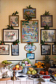 Geflieste Anrichte, gefüllt mit festlichen Früchten vor einem Hintergrund aus mit Stechpalmen geschmückten Bildern
