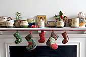 Festive mantlepiece decorated with crockery holly and colourful christmas stockings