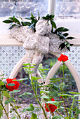 Red geraniums by Victorian window with white angel topped with bay foliage