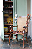 Can chair in kitchen corner with open cupboard door displaying tableware and crockery