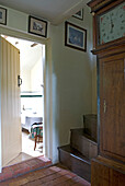 Open door to bathroom from hallway with wooden staircase and grandfather clock