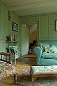 Zeitschriftenregal auf Hocker und Sofa in grün getäfeltem Landhaus-Wohnzimmer