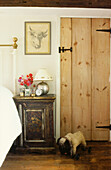 Bedside table with lamp below portrait of bull's head and panelled wooden bedroom door