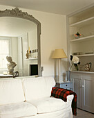 White sofa in living room with oversized mirror reflecting bust of Caesar and original Edwardian wall cupboard 