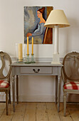 Grau gestrichener Tisch mit Lampe und zu den Kunstwerken passenden Stühlen, die mit roten Karos gepolstert sind