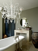 Atelier wirework Neo-Baroque chandelier hanging above roll top bath in neutral grey and stone tiled bathroom