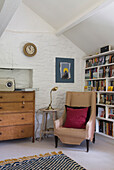 Armchair and lamp with chest of drawers in whitewashed attic room