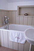 Badezimmer mit feuchtigkeitsbeständiger Wandvertäfelung mit Schilfrohr, Duscharmatur und Handtuch mit Monogramm auf der Badewanne