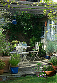 Patio area in back garden with white ornamental metal garden furniture and blue glass lantern hanging from rustic arbour