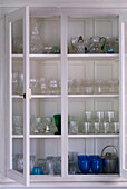 White painted dresser with open doors displaying a collection of glassware on shelves