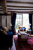 Living room in period cottage with blue velvet sofa and curtains and Persian rug