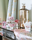 Stack of china cups and floral patterned tea kettle next to floral print fabric