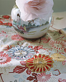 Vase mit Rose auf Tischtuch mit Blumendruck