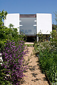 Fußweg mit blühendem Garten und modernem Haus im Hintergrund