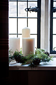 Three church candles with pine cones on windowsill with leaded panes