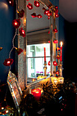 Angezündete Kerzen und Lichterketten auf einem metallgerahmten Spiegel in einem dunklen Raum