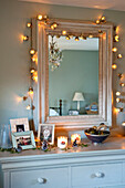 Family photographs on chest of drawers under mirror with lit fairy lights
