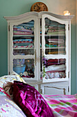 glass fronted linen cupboard and fuchsia covered cushion in pastel green bedroom