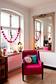 Upholstered pink chair in a living room with a large window and mirror