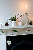 Lit candle and pinecones with glass ornaments on original fireplace of London home 