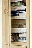 Glassware and folded linen in built-in storage cupboard Devon