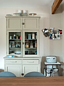 Glass fronted kitchen dresser and high chair in kitchen of Suffolk home England UK