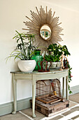 Solar gilded convex mirror and houseplants on demi-lune table in Canterbury home England UK