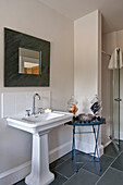 Square framed mirror hangs above pedestal basin with glassware in bathroom of Canterbury home England UK