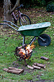 Wheelbarrow and bicycle with burning logs in wrought iron garden stove Yeovil Somerset, England, UK