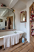 Mirror over freestanding bath with kimono hanging on back of door in UK home